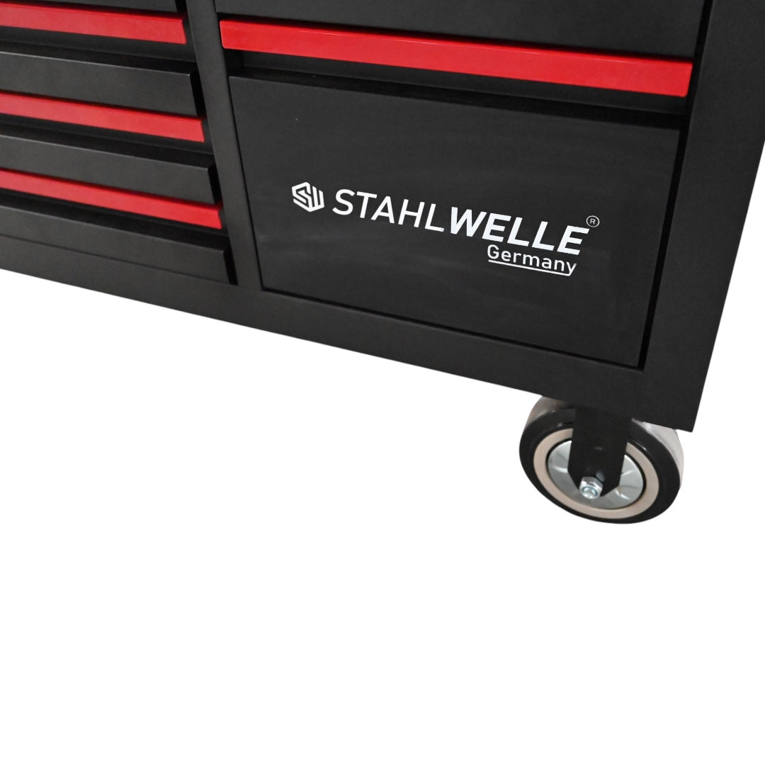 Een complete Stahlwelle SG11 werkplaatsinrichting, schuin van voren gefotografeerd tegen een witte achtergrond. De set bestaat uit een zwarte gereedschapswagen met meerdere laden voorzien van rode accenten en handgrepen, een houten werkblad, een geperforeerde achterwand voor gereedschapshaken en een bovenkast met twee deuren. De inrichting staat op wielen voor mobiliteit en biedt uitgebreide opbergruimte en een werkplek voor een werkplaats of garage.